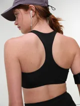 Top deportivo negro con espalda nadadora, copas removibles y detalle de logo sutil en el elástico inferior.