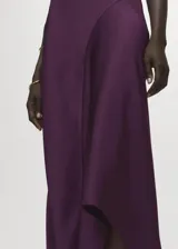 Vestido midi de satén color violeta oscuro, con diseño drapeado en el escote y un hombro al descubierto, de manga corta caída y bajo asimétrico.