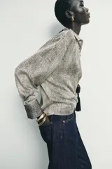 Camisa de manga larga con cuello solapa y cierre frontal de botones. Presenta un estampado de puntos pequeños en tono crema y negro, con puños en contraste que incluyen un estampado más denso.