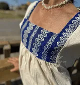Túnica de lino color crudo con corte holgado y mangas cortas. Presenta una pechera cuadrada en el frente y la espalda confeccionada con textiles antiguos en color azul con patrones geométricos de ondas.