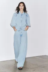 Camisa de denim celeste con cuello solapa, manga corta abullonada y cierre frontal con botones.