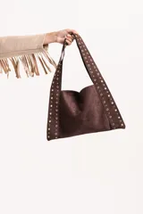 Cartera tipo hobo de gamuza color marrón, con diseño de tiras laterales decoradas con tachas metálicas doradas. Cuenta con una correa única integrada al diseño.