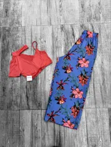 Conjunto de top corto y pantalón palazzo con estampado floral. El top es de color coral con un diseño asimétrico de un solo hombro. El pantalón es de color azul con estampado de flores rojas y hojas verdes.