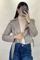 Chaqueta corta tipo biker confeccionada en gamuza color beige, con cierre frontal cruzado, solapas amplias, bolsillos con cierre y cinturón ajustable en la cintura.