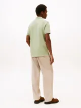 Chomba verde claro de corte regular, confeccionada en tejido piqué de algodón orgánico con un toque de elastano. Tiene cuello tipo chomba, cartera de dos botones y logo de Tommy Hilfiger bordado en el pecho.