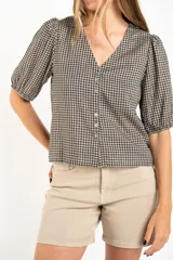 Blusa de algodón con estampado de cuadros vichy en tonos negro y blanco. Presenta escote en V, cierre frontal con botones y mangas cortas abullonadas con terminación elástica.