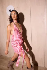 Vestido corto de gasa con estampado de rayas verticales rojas y blancas. Posee un escote pronunciado, espalda descubierta y detalle de drapeado lateral con un lazo largo multifuncional.
