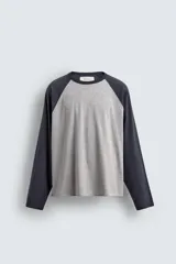Camiseta de corte relajado con diseño color block, cuerpo en gris melange y mangas largas raglán en color azul marino. Presenta cuello redondo al tono de las mangas y bajo con acabado irregular.
