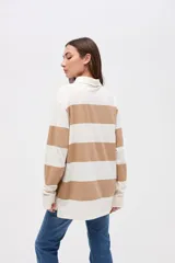 Remera tipo polo de manga larga con diseño de rayas horizontales anchas en bloques de color crema y beige. Presenta cuello camisero con cierre de botones y un pequeño bordado en el pecho.