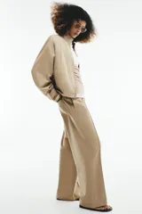 Cazadora bomber de color beige con cuello subido, manga larga y bolsillos delanteros. Cuenta con cierre frontal de cremallera metálica y cordón ajustable en el dobladillo.