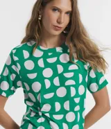 Blusa de viscosa con cuello redondo, manga corta y diseño con nudo lateral. Presenta un estampado geométrico de semicírculos blancos sobre fondo verde.