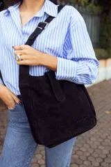 Bolso negro de cuero gamuzado con correa larga regulable y logo de la marca grabado en el frente.