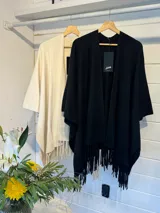 Ruana color crema con flecos en los bordes, de diseño abierto y holgado.