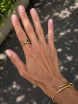Anillo de acero dorado con diseño cruzado de líneas curvas y acabado brillante.