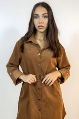 Sobre camisa de gamuza sintética color tabaco, con cuello camisero, cierre frontal de botones metálicos, mangas largas con puños abotonados y cinturón ajustable con hebilla metálica en la cintura.