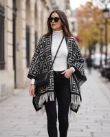 Poncho de lana negro y blanco con diseño geométrico y flecos en el borde inferior.