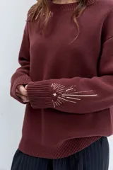 Sweater de punto color bordó, con cuello redondo, manga larga y diseño holgado. Presenta detalles bordados en hilo dorado en la zona del hombro y en el puño.