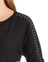 Blusa de tejido acanalado con cuello redondo y mangas tres cuartos. Presenta detalle de tachas metálicas a lo largo de los hombros y mangas, con puños elastizados.