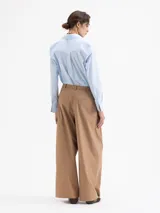 Pantalón negro de poplín asargado, corte holgado y tiro alto con pliegues frontales. Presenta un cruce en la cintura que genera un cinturón con gancho.