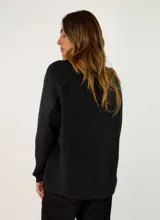 Sweater de punto con escote en V, manga larga y corte holgado. Presenta un diseño liso con costura central vertical en el frente y terminaciones acanaladas en puños y ruedo.