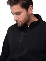 Buzo negro de corte clásico con cuello alto y cierre frontal parcial. Presenta logo vertical grabado en el pecho, bolsillo frontal tipo canguro y puños y cintura de punto elástico.