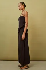 Vestido largo de color negro con escote recto y tirantes finos ajustables. Presenta un diseño con detalle de volante tipo peplum en la cintura y falda con caída fluida.