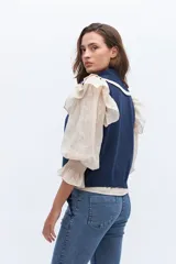 Chaleco de punto sin mangas, color azul marino, con cuello y frente adornados con volados en contraste de color blanco o crudo.