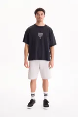 Remera oversize de manga corta en color negro con efecto acid wash. Presenta un pequeño estampado frontal con texto en inglés y un isotipo de flor en la parte superior del pecho.