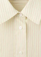 Camisa oversize color beige con sutiles rayas verticales, cuello camisero y cierre frontal con botones.