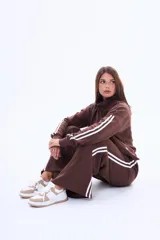 Buzo de felpa color marrón con medio cierre frontal, cuello alto y mangas largas con dos franjas blancas laterales.