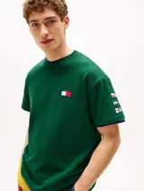 Remera verde de algodón con cuello redondo y corte amplio. Presenta el logo de Tommy Hilfiger en el pecho y un logo oversize en la parte trasera. Tiene mangas cortas con hombros caídos y un parche con logo en la manga.