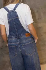 Enterito de denim azul con silueta relajada, breteles regulables, peto con bolsillo frontal y piernas rectas con tajos laterales en el ruedo.