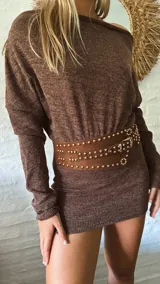 Vestido corto de punto color marrón, con escote tipo bote que deja los hombros al descubierto y mangas largas. El diseño es ajustado al cuerpo.