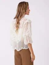 Blusa Liv Los Angeles confeccionada en tul bordado color beige, de cuello alto, cierre frontal con botones y mangas tres cuartos con terminación amplia.