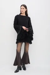 Sweater negro de lana merino con silueta amplia y relajada. Presenta mangas acampanadas con volumen, decoradas con volados de lino y terminaciones de flecos en los puños y en el ruedo.