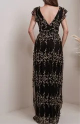 Vestido largo de fiesta confeccionado en malla negra con bordados florales en hilo dorado. Presenta un escote en V profundo, mangas cortas con volados y una cintura definida.