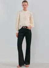 Blusa color crudo con cuello alto, detalles de bordados verticales en el frente y mangas largas abullonadas con puños ajustados.