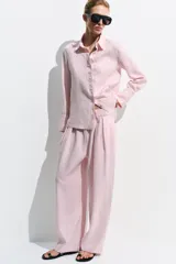 Pantalón de tiro medio confeccionado en 100% lino color rosado, con diseño de pernera ancha, pinzas en el delantero, cintura elástica en la parte posterior y bolsillos laterales. Cuenta con cierre frontal con cremallera y botón.