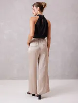 Pantalón palazzo de tiro alto confeccionado en tela satinada. Presenta una pretina delantera con pasadores, cierre y broche, mientras que la parte trasera cuenta con elástico para mayor comodidad. Incluye bolsillos verticales en el frente.