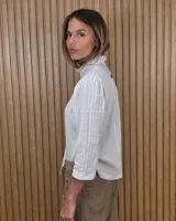Camisa de algodón color blanco, con cuello alto con volados, mangas tres cuartos con detalles de bordado ingles y cierre frontal con botones de nácar.