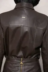 Campera de cuero color marrón con cuello clásico, cierre frontal con botones metálicos y detalles de volados en gamuza a lo largo de la botonadura y en los puños.