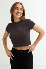 Remera crop top de manga corta, color gris oscuro, con cuello redondo y texto estampado en tono similar que dice "My heart says yes my brain says no".