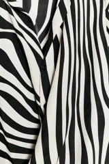 Camisa de manga larga con estampado de cebra, cuello solapa, escote en pico y cierre frontal con botones. Presenta un diseño con nudo en el bajo delantero y puños abotonados.