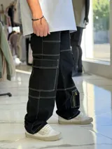 Pantalón cargo de jean negro con múltiples bolsillos utilitarios y costuras visibles en contraste de color blanco.