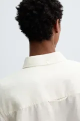 Camisa de corte relajado confeccionada en tejido de cáñamo, color blanco. Presenta cuello de solapa, manga larga con puños abotonados y cierre frontal de botonadura.