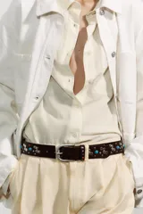 Cinturón de cuero negro con tachas plateadas, rojas y turquesas. Hebilla metálica plateada ovalada.