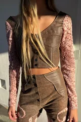 Top de cuero color marrón con mangas largas de encaje rosado. Presenta un diseño entallado con escote en V, costuras decorativas frontales y cierre mediante botones metálicos.