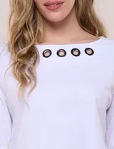 Remera blanca de algodón con elastano, de corte semi holgado, escote bote con ojalillos metálicos frontales, mangas tres cuartos raglán y ruedo asimétrico curvado.