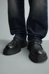 Mocasín negro de cuero liso con detalle de antifaz en el empeine y suela track gruesa y dentada.