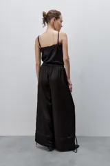 Pantalón de pierna amplia y calce holgado, color negro, confeccionado en tejido satinado. Cuenta con cintura elastizada, recortes horizontales y tiras regulables en los ruedos.
